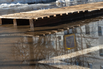 Pallet in a puddle in spring, reflection of a crosswalk sign in the water