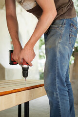 Skilled young male worker is using power screwdriver drilling during construction wooden bench, do it yourself