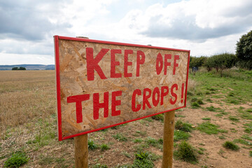 Oxfordshire, England, UK. 2021. A farmers hand painted sign in red paint saying, keep off the crops ! I a field in Cotswolds area of the UK.