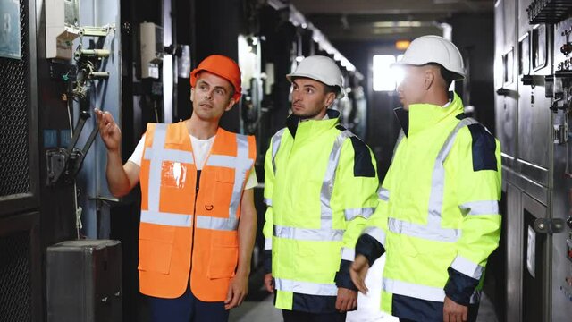 Engineers in uniform and helmets do pre-commissioning works inspecting electrical station. Group of three engineer team with perfect safety uniform brainstorming idea planning project of industry.