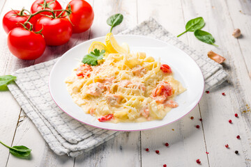 fettuccine with salmon and tomatoes on white plate on white wooden table