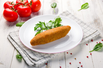 chicken Kiev cutlet with greens on white plate on white wooden table