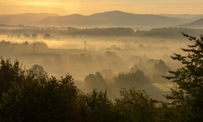 Obraz na płótnie Canvas View of the valley full of fog during sunrise, with mountains in the background