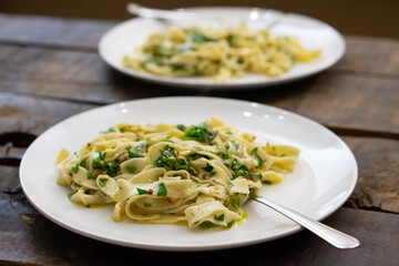 Selective focus shot of delicious plates of fresh pasta with greens on white plates on wooden table