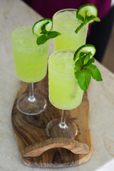 Refreshing green drinks with cucumber and mint in stemmed glasses on wooden serving board