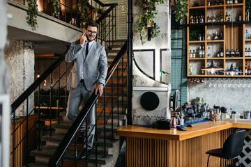 A middle-aged businessman stands on the steps in a cafe and talks on the phone.