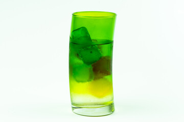 Colorful ice cubes and water in green glass cup on white background