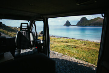 View from inside of camper van on beautiful beach with turquoise water and mountain cliffs. Adventure camping life vibes. Vanlife lifestyle in scandinavian landscape. Interior of converted camper van