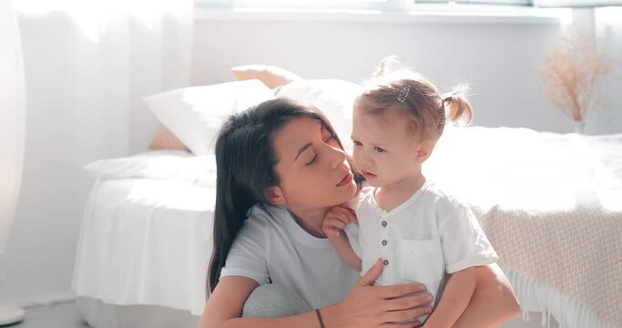 Mom with her little daughter at home. Woman kisses, hugs and soothes the child