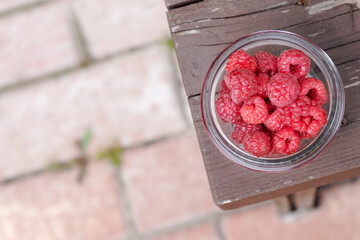 raspberries in a glass bowl. wooden brown background