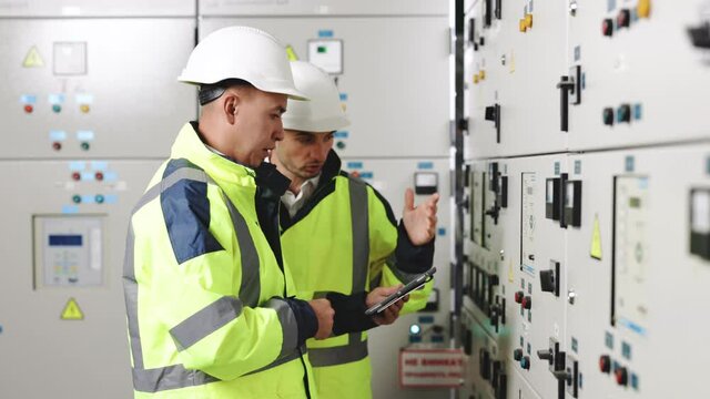 Electrical engineers checking control panel board with tablet. High voltage power station. Electrical engineers standing near therminal box of solar panel