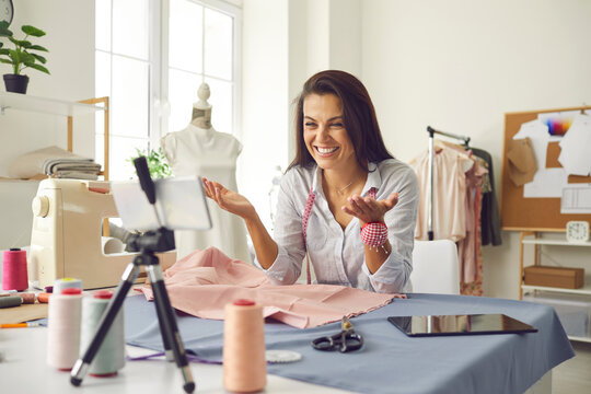 Woman smiling at camera giving subscriber virtual online lesson workshop on making modern custom clothes. Creative fashion channel blogger shares professional skill, experience, knowledge, work advice
