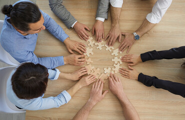 Diverse business people team group joining puzzle pieces sitting at office desk table view from top above. Collaboration and cooperation strategy, teamwork and teambuilding concept