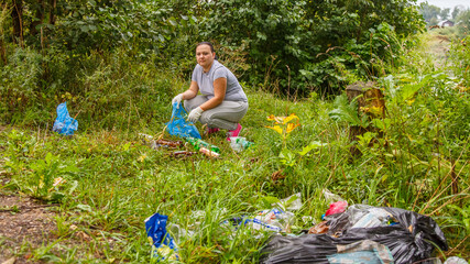 A woman volunteer cleans up garbage at a dump in nature.