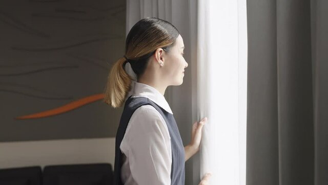 The hotel maid is closing the curtains to keep the hotel room tidy.
