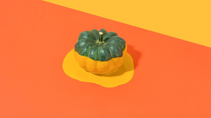 Minimal composition with half painted dark green  pumpkin and orange liquid on bright red table....