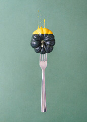 Creative composition with silver fork and dark pumpkin dipped in yellow liquid paint against green background.