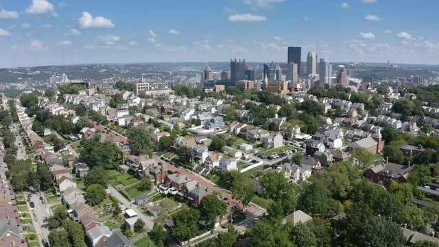 A slow orbiting summer aerial establishing shot of a Mount Washington residential neighborhood overlooking the city of Pittsburgh.  	