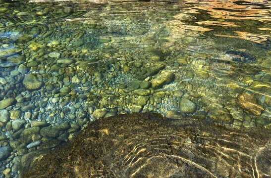 Green transparent sea water on pebble beach. Clear sea water background. Pebbles, stones, gravel on seabed. Beautiful seascape.