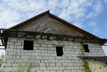 abandoned private white brick house with empty windows with gray wooden loft on a background of blue sky and clouds