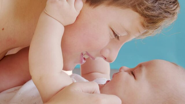 Boy kissing newborn ssister lying together on bed at home. Portrait of adorable baby and toddler boy siblings playing and relaxing. Childhood and family concept.