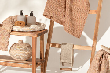 Fototapeta na wymiar Natural waffle linen towels in earth tones on wood bench and towel ladder with bamboo toothbrushes, rattan baskets, and soap dispenser. Daily body care, spa and wellness zero waste bathroom concept
