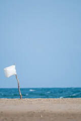 Vertical image of deserted beach with a white flag made of a wooden stick stuck in the sand and a...