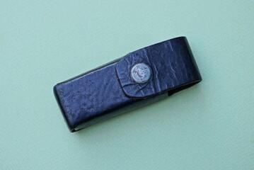 one black leather closed tool case with a gray metal button lies on a green table