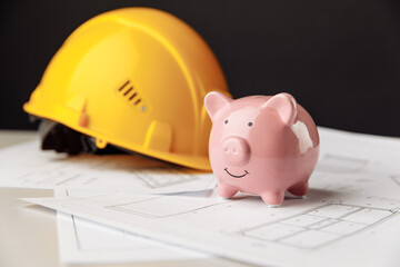 Building costs concept. Yellow safety helmet and pink piggy bank with drawings