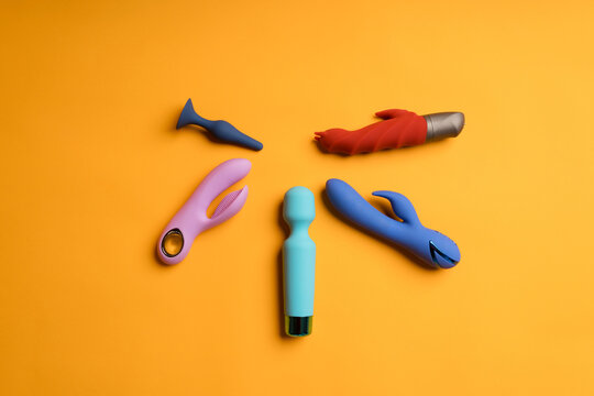 An abundance of colorful dildos on a yellow background. Clitoral massager, sex toys for maintaining women's health