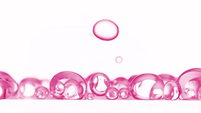 Macro shot of pink clear different sized bubbles are falling down to another ones on white background | Abstract skin care cosmetics with retinol formulation concept