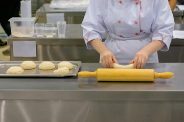 Baker, chef hands kneading fresh dough on round wooden board on kitchen table at cuisine of restaurant, bakery - close up. Professional cooking, gastronomy, pastry and food concept