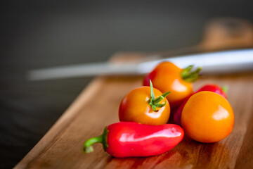 Small ripe tomatoes and red chilly peppers placed on wooden cutting board with a knife out of focus on the background
