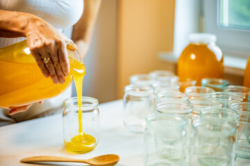 Woman pours honey into transparent jars on a white table