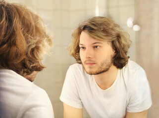 young man looking in the mirror,combing his hair,looking at problems on face