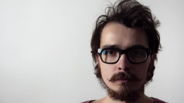 Portrait of young bearded man with mustache wearing glasses standing on white background. Closeup view of male unshaved caucasian person with serious face. Thoughtful smart hipster looks at the camera