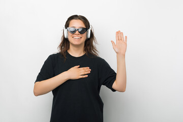 Young woman is making the promise or swear gesture while wearing headphones and sunglasses over...