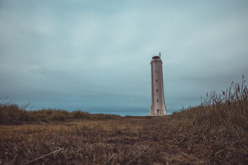 Fototapeta na wymiar Panoramic view of Malarrif lighthouse on the east of iceland on a cloudy day. Tall Lighthouse in iceland in grey color and thick clouds above.