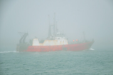 Fishing boat sailing in the ocean through dense fog