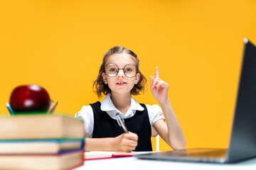 Serious schoolgirl raises finger up. Sitting at the desk with laptop in glasses. Distance education 