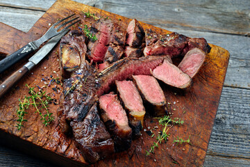 Rustic traditional barbecue dry aged wagyu porterhouse beef steak bistecca alla Fiorentina sliced and served as close-up on a wooden board
