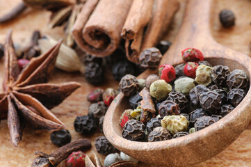 Grains of different peppers in a wooden spoon, anise stars, cinnamon sticks and cloves on a wooden...