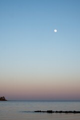 Sunset over bay. Moon shining in the sky.