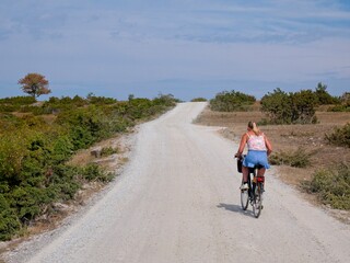 Blonde woman cycle on gravel road on Öland, Sweden.