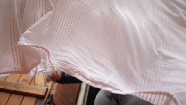 Woman shaking blanket outside removing dust from bedsheet