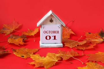 Calendar for October 1: decorative house with the name of the month in English, the numbers 01, yellow autumn maple leaves scattered on a red background