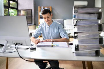 Obraz na płótnie Canvas Young Businessman Working At Office With Stack Of Folders