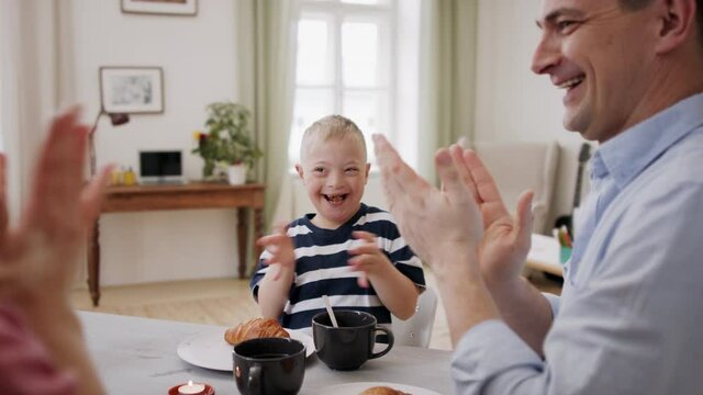 Happy family with down syndrome son at the table, having breakfast and fun.