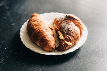 Continental breakfast concept. Croissants with cream on a white plate and dark background