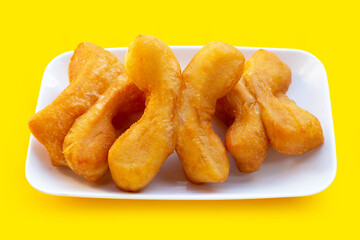 Deep-fried dough sticks or chinese bread sticks in white plate on yellow background.